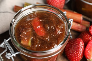 Photo of Jar of tasty rhubarb jam, fresh stems and strawberries on table, closeup