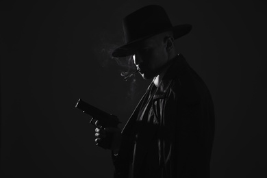 Photo of Old fashioned detective with gun smoking cigarette on dark background, black and white effect