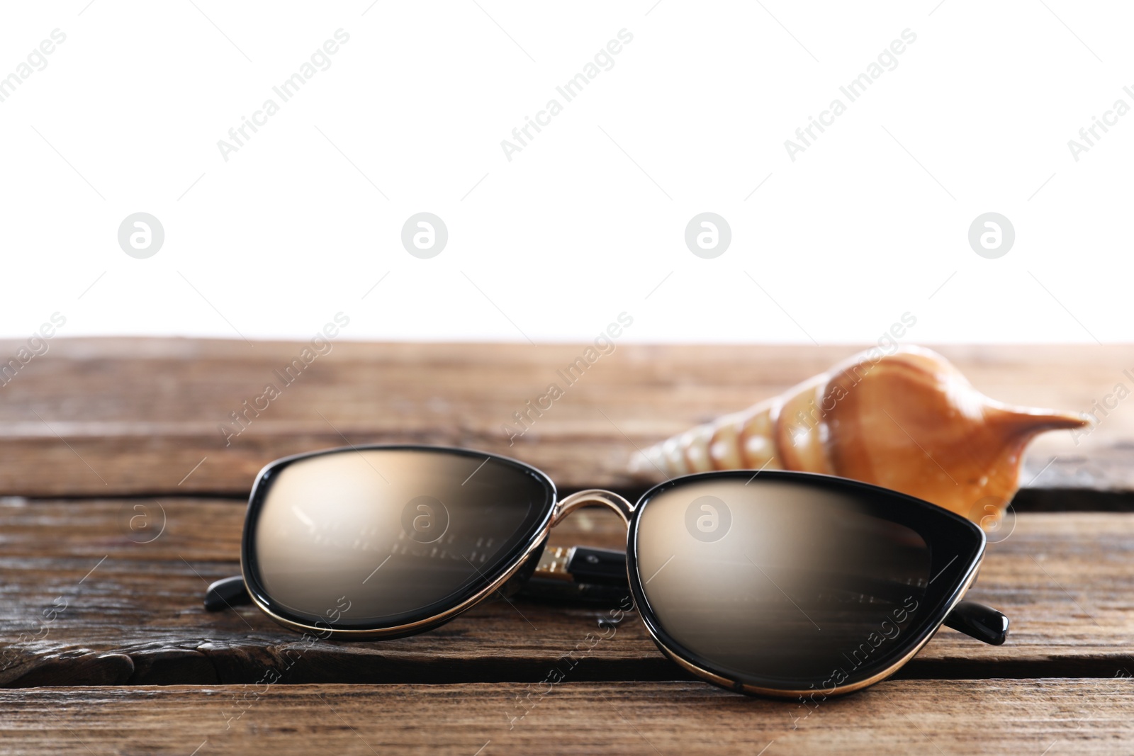 Photo of Stylish sunglasses and shell on wooden table against white background