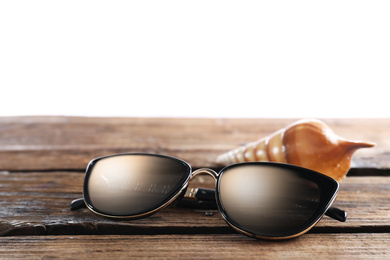 Stylish sunglasses and shell on wooden table against white background