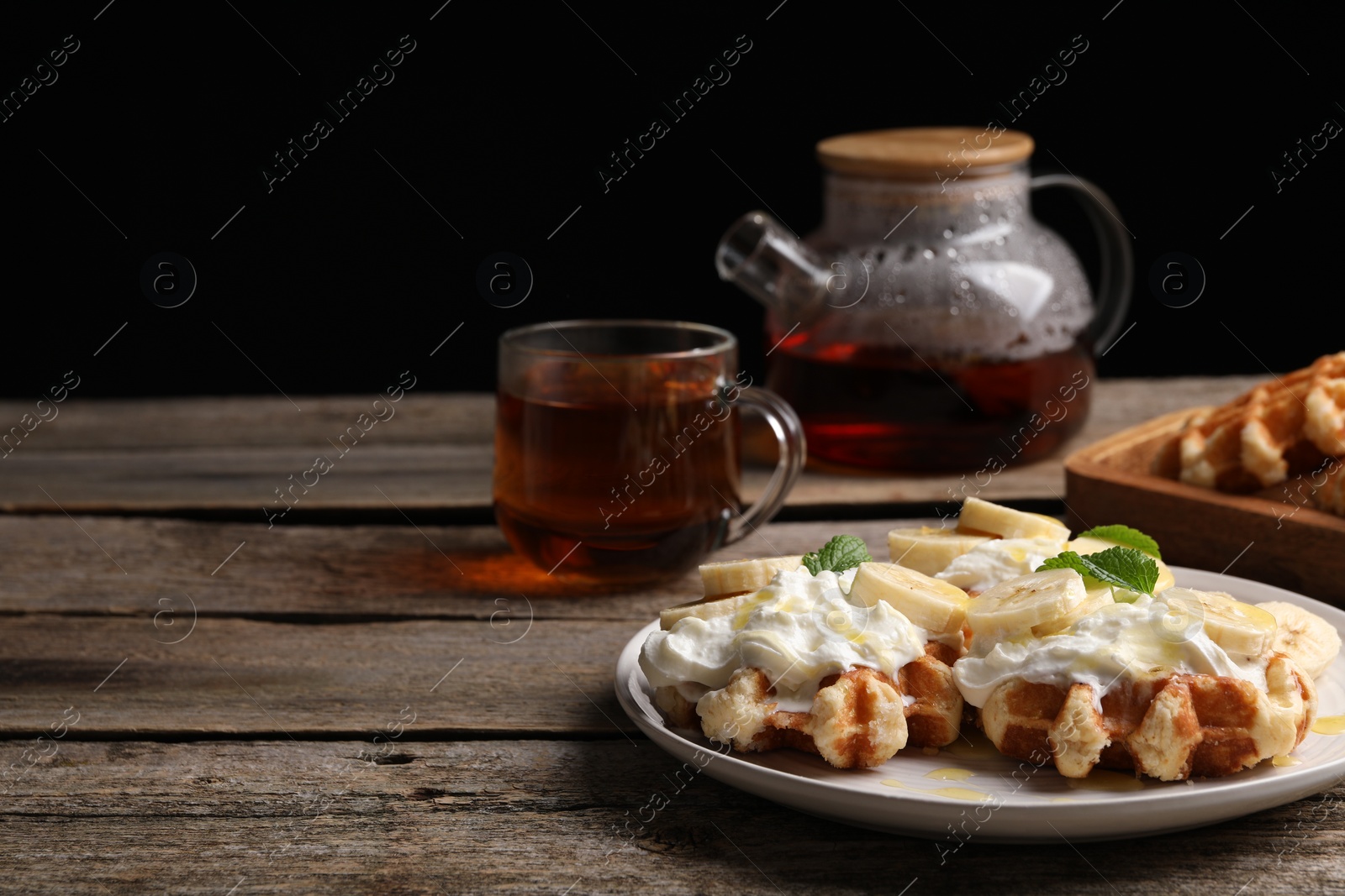 Photo of Delicious Belgian waffles with banana and whipped cream served on wooden table, space for text