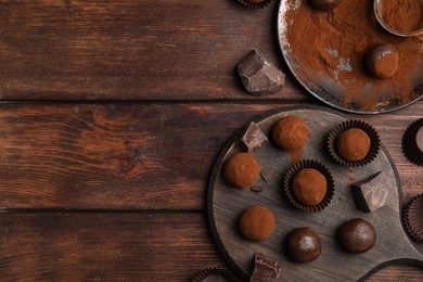 Photo of Delicious chocolate truffles powdered with cocoa on wooden table, flat lay. Space for text
