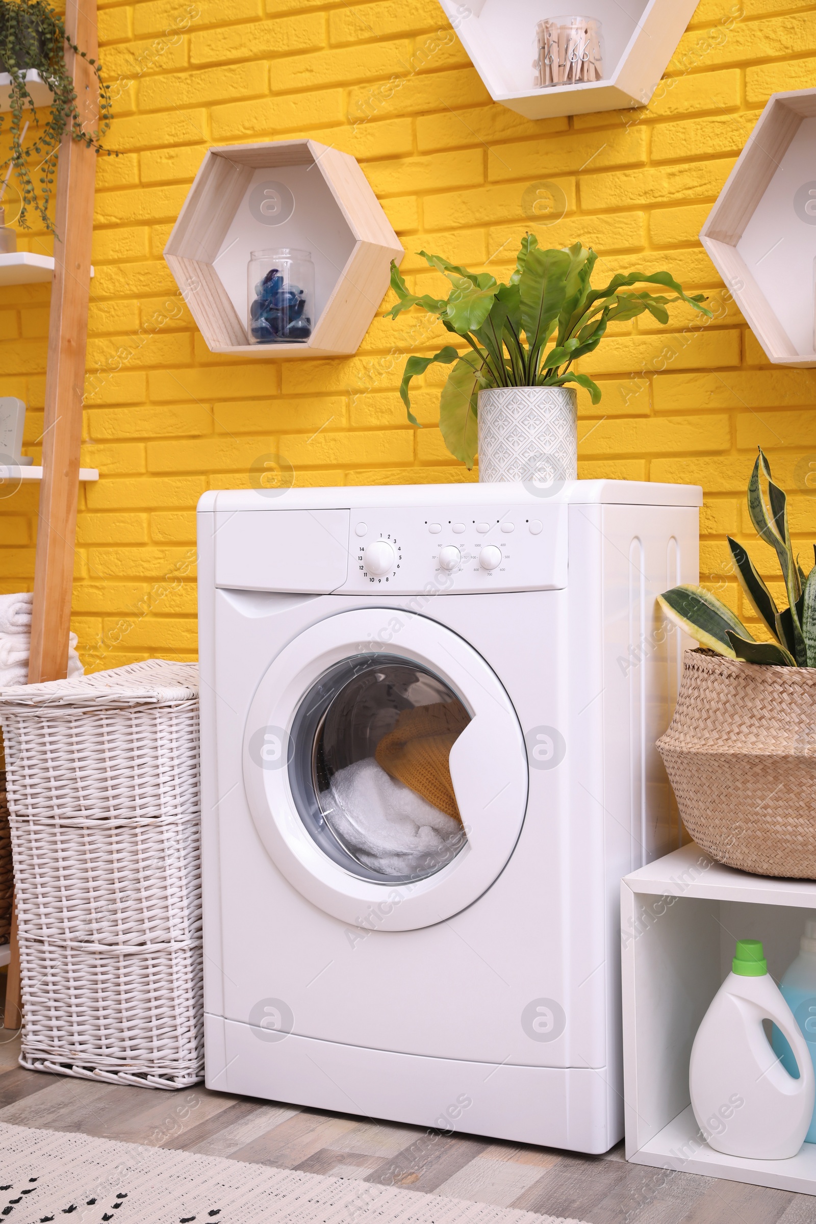 Photo of Laundry room interior with modern washing machine near yellow brick wall