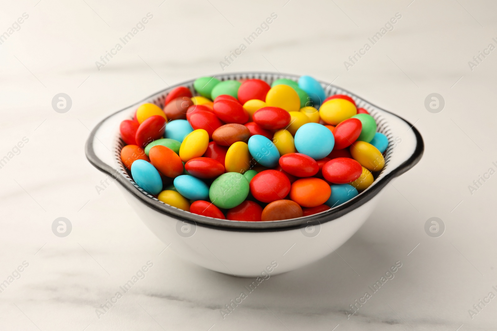 Photo of Bowl with tasty colorful candies on white marble table, closeup