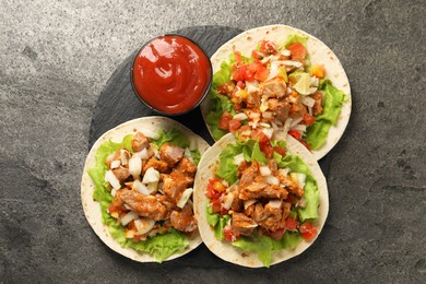 Delicious tacos with vegetables, meat and ketchup on grey textured table, top view