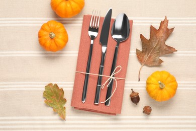 Photo of Cutlery, napkin and autumn decoration on tablecloth, flat lay. Table setting