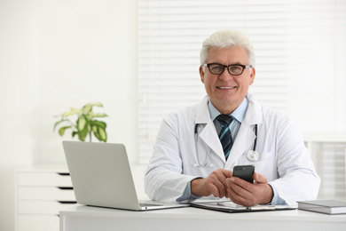 Senior doctor with smartphone at table in office