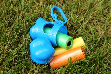 Photo of Rolls of colorful dog waste bags on green grass outdoors, above view