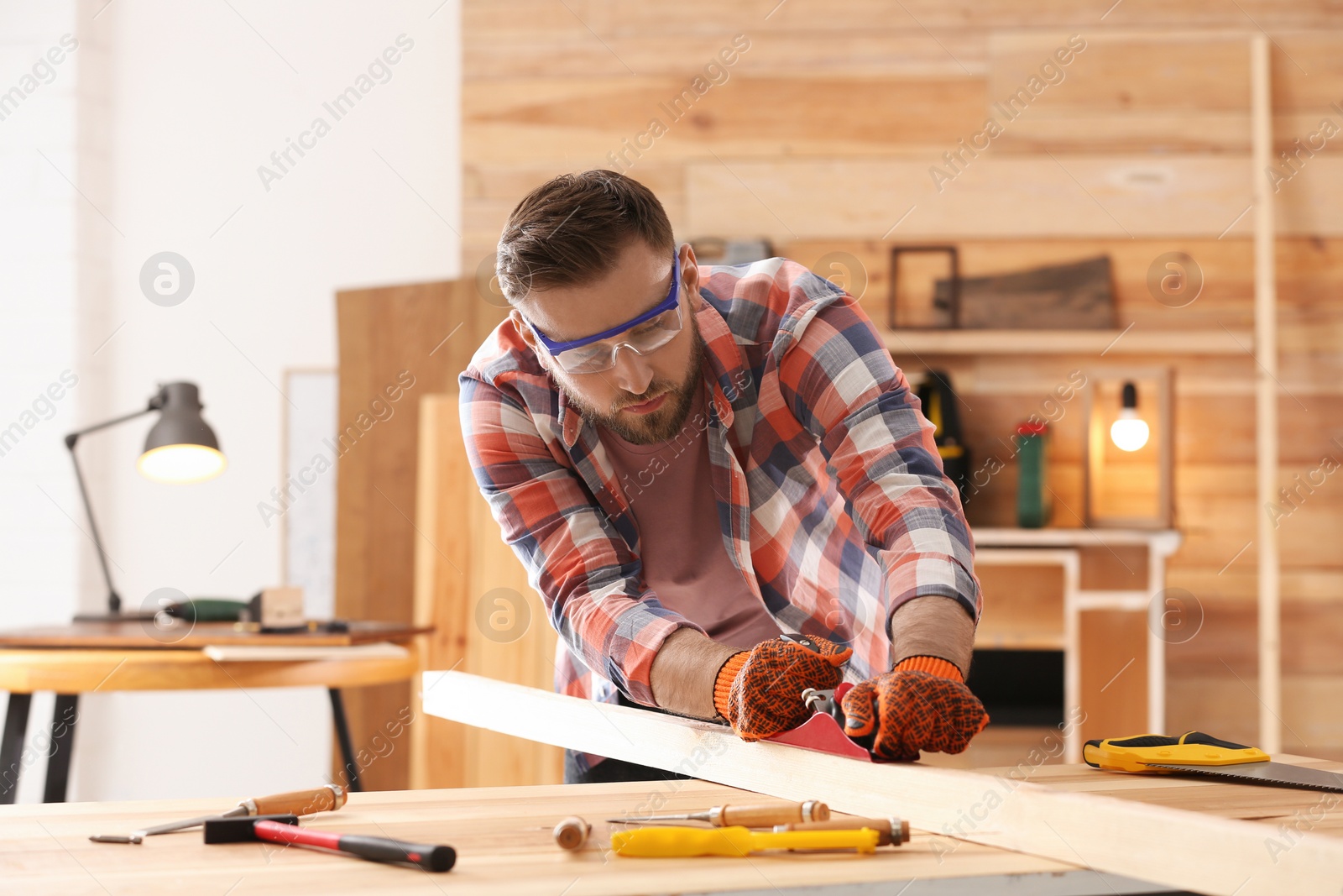 Photo of Carpenter shaping wooden bar with hand plane at table in workshop