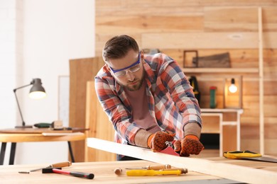 Carpenter shaping wooden bar with hand plane at table in workshop