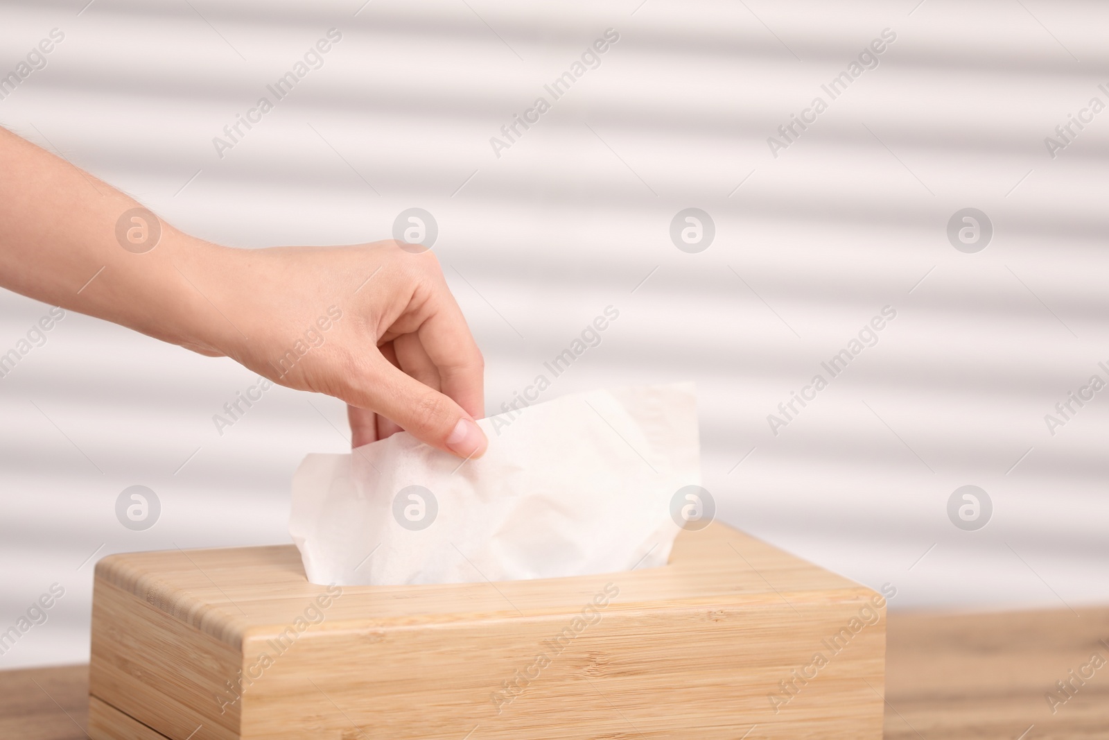 Photo of Woman taking paper tissue from holder on light background, closeup