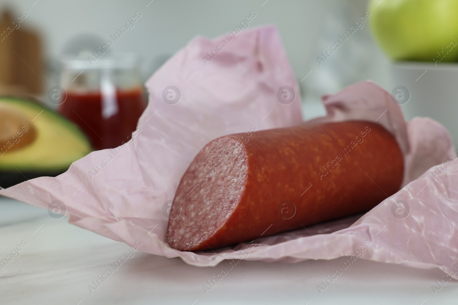 Photo of Fresh tasty sausage in beeswax food wrap on white marble table, closeup