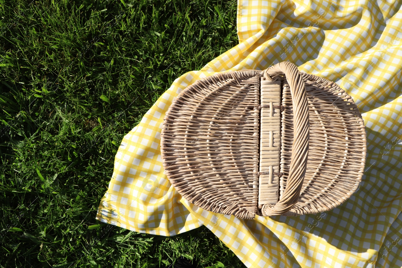 Photo of Picnic basket with checkered tablecloth on green grass, top view. Space for text