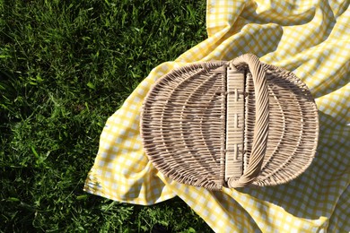 Photo of Picnic basket with checkered tablecloth on green grass, top view. Space for text