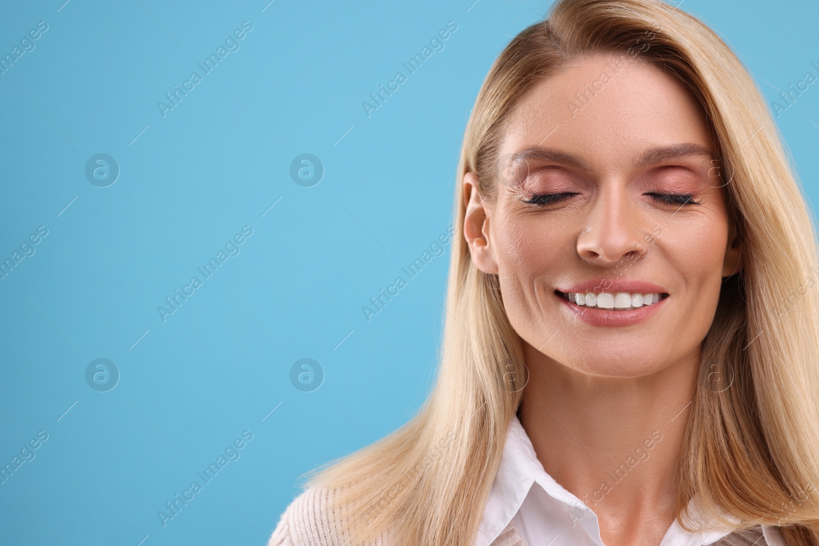 Photo of Portrait of smiling middle aged woman on light blue background. Space for text