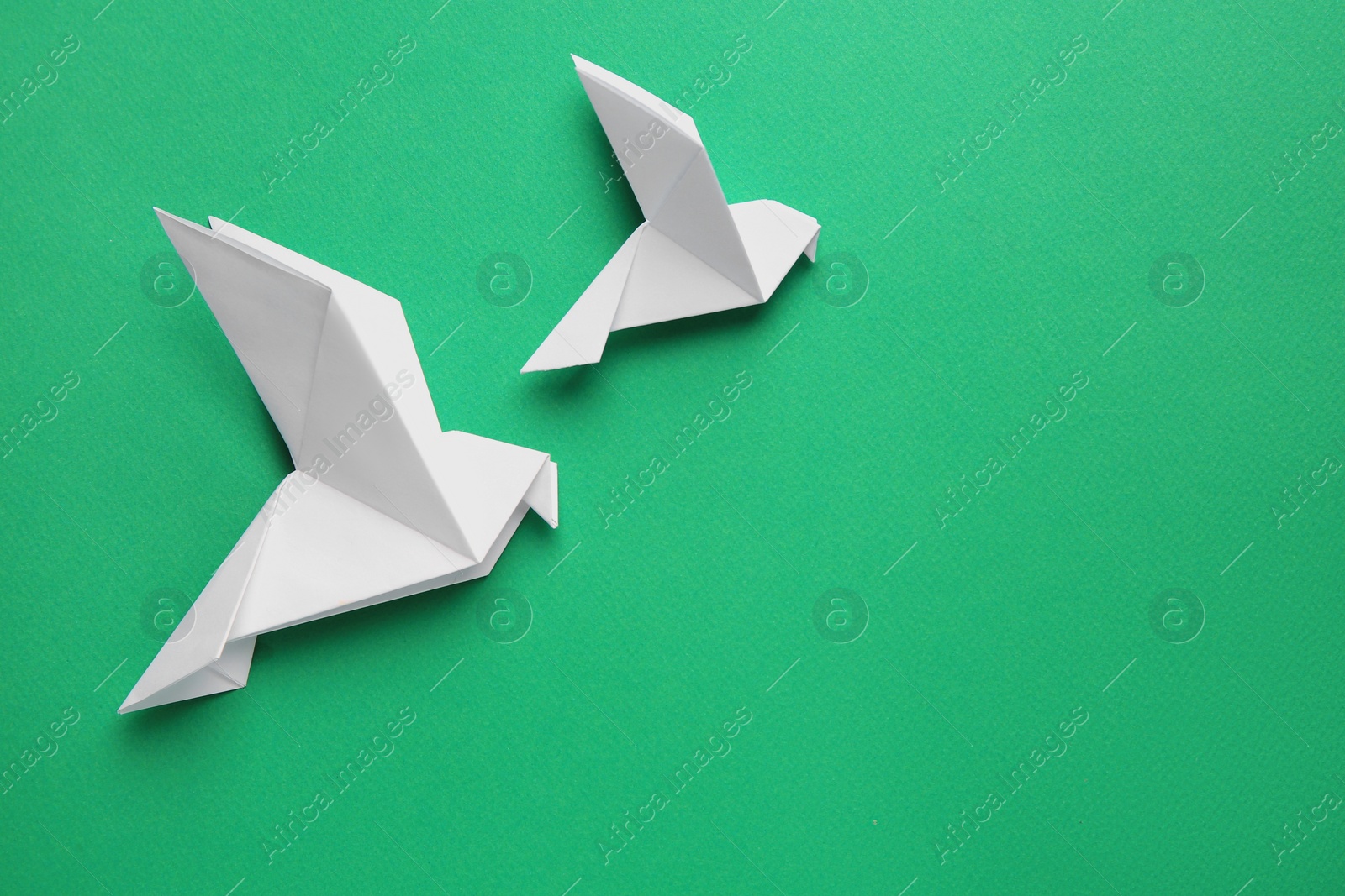 Photo of Beautiful white origami birds on green background, flat lay. Space for text