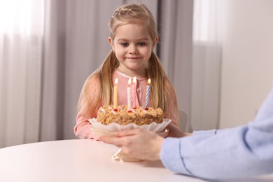 Birthday celebration. Mother holding tasty cake with burning candles near her daughter indoors