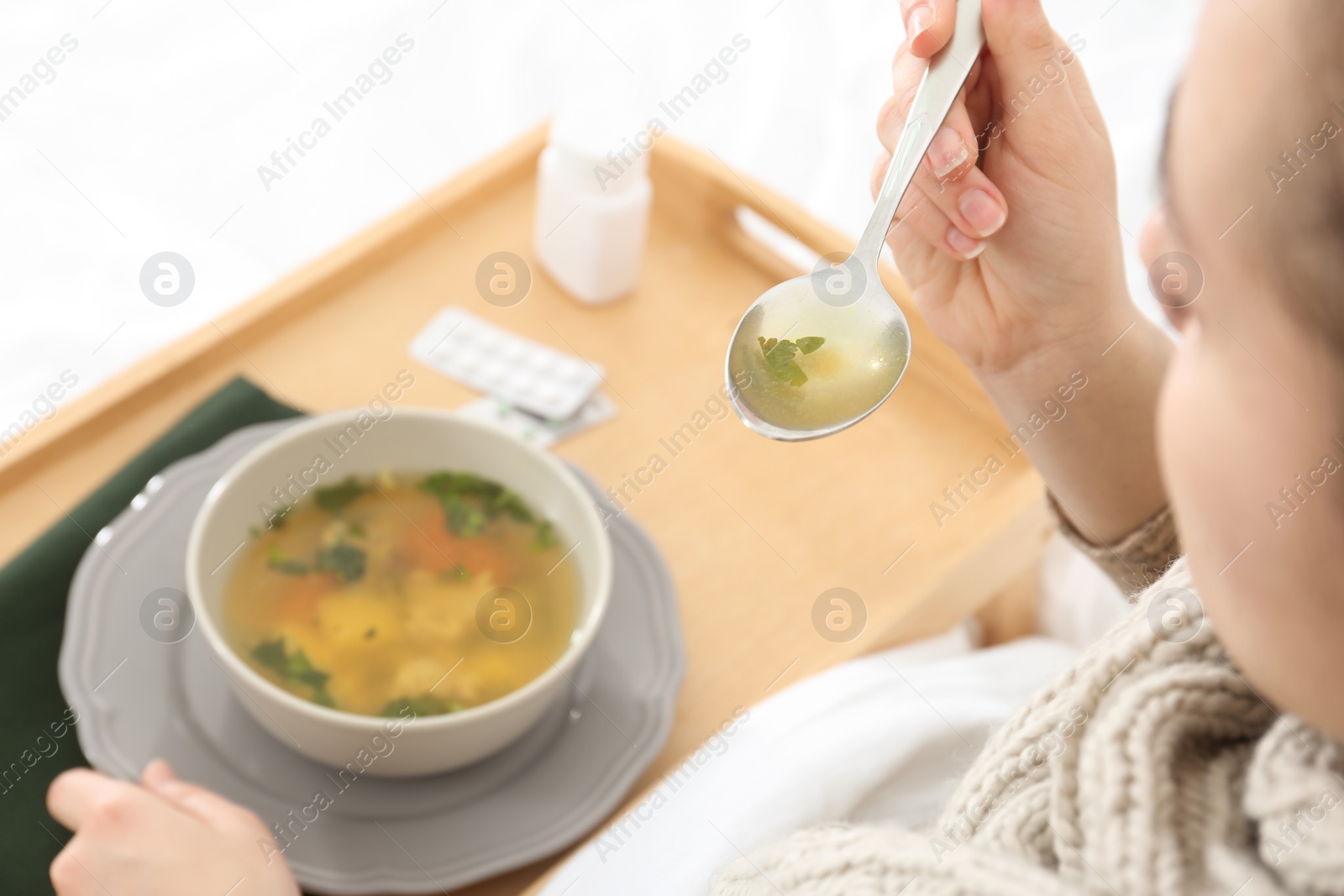 Photo of Sick young woman eating broth to cure cold in bed, closeup