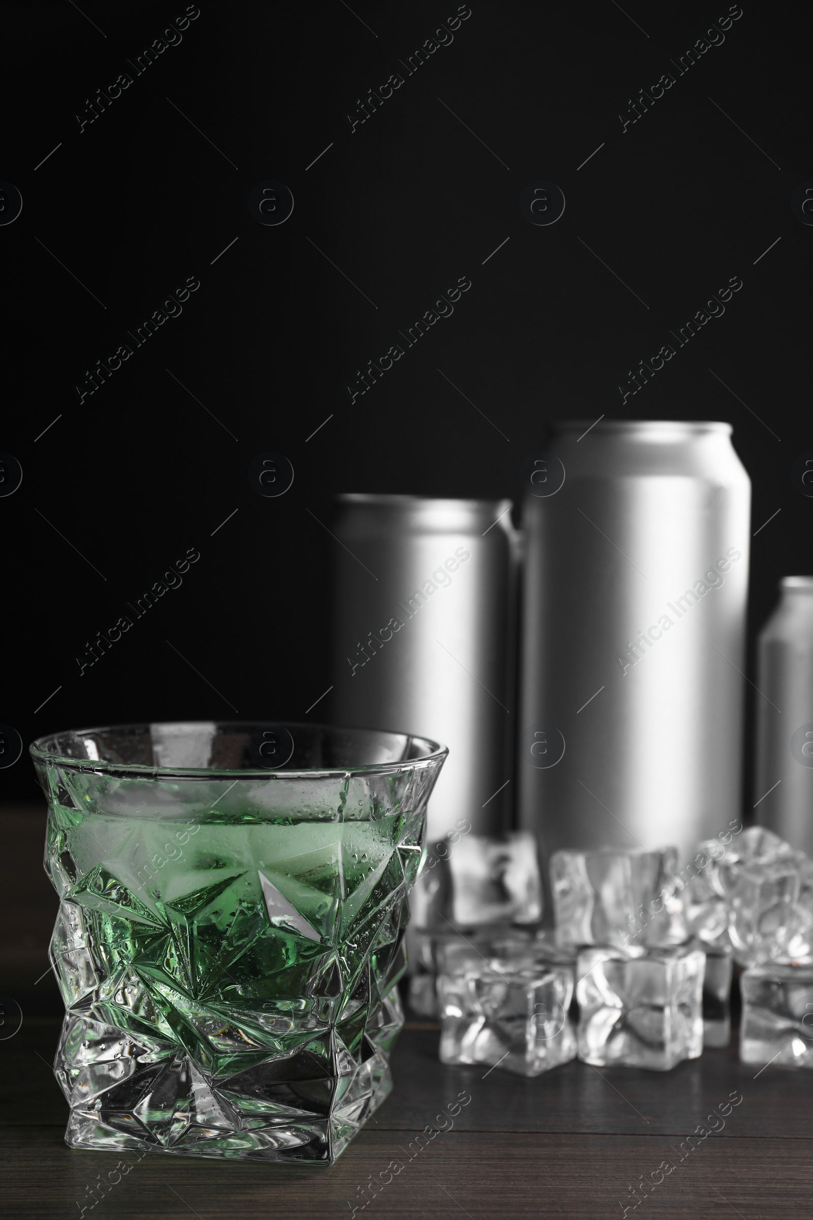 Photo of Energy drink in glass, aluminium cans and ice cubes on wooden table