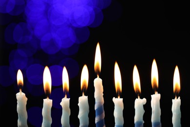 Photo of Hanukkah celebration. Burning candles against dark background with blurred lights, closeup