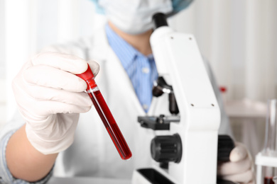 Photo of Scientist holding test tube with blood sample in laboratory, closeup. Virus research