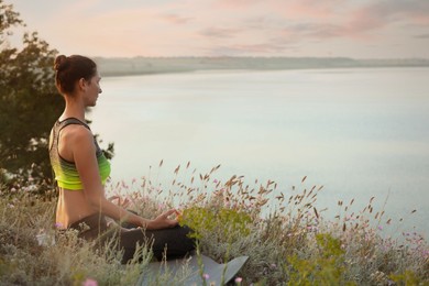 Photo of Woman meditating in meadow near river. Space for text