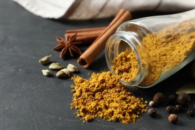 Jar with dry curry powder and other spices on dark textured table, closeup. Space for text