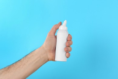 Man holding nasal spray on light blue background, closeup