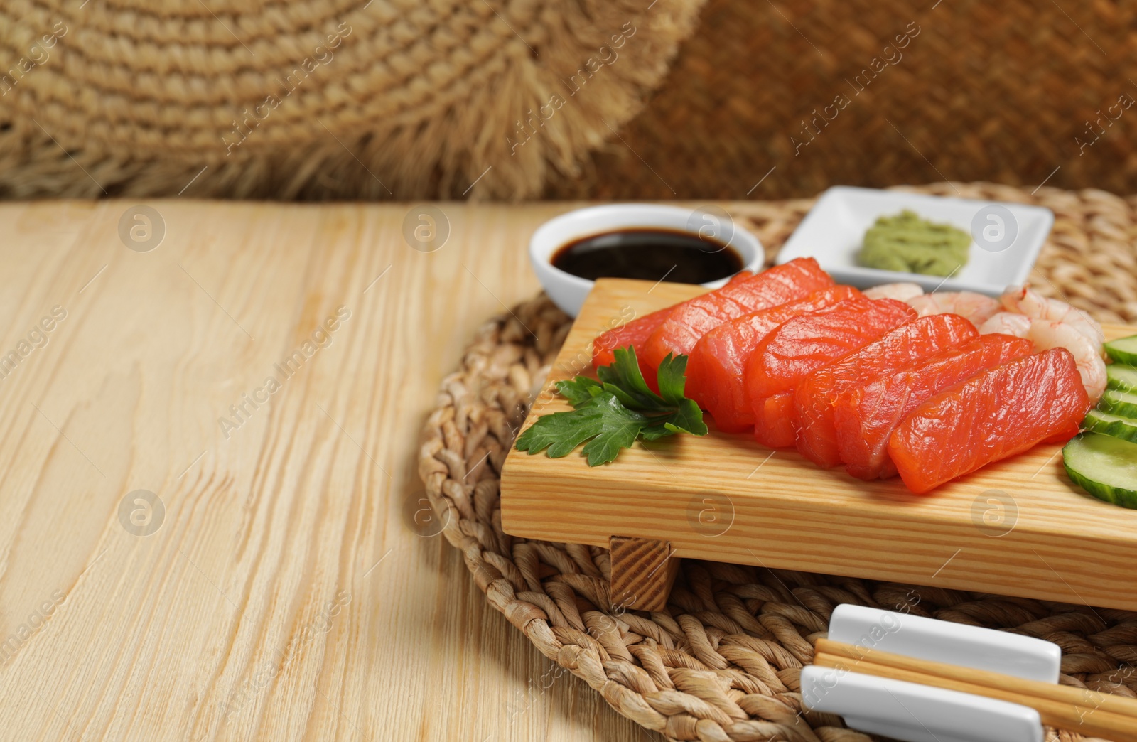 Photo of Delicious sashimi set of salmon and shrimps served with cucumbers, parsley and soy sauce on wooden table. Space for text