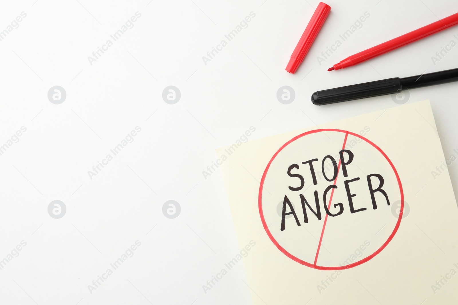 Photo of Black and red felt tip pens near sheet of paper with crossed over inscription Stop Anger on white background, flat lay. Space for text