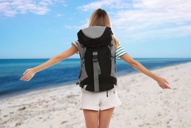 Traveler with backpack on seashore during summer vacation trip, back view