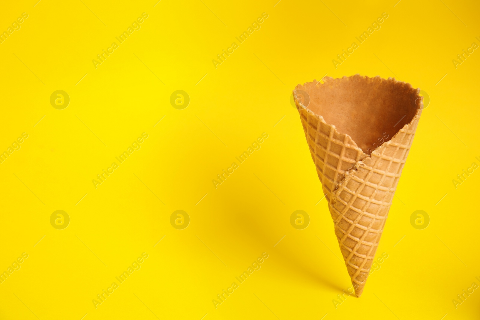 Photo of Empty wafer ice cream cone on yellow background. Space for text