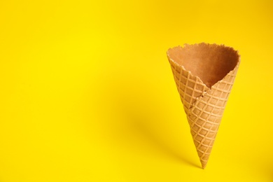 Empty wafer ice cream cone on yellow background. Space for text