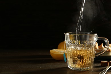 Photo of Pouring hot water into glass cup with tea bag at dark wooden table. Space for text