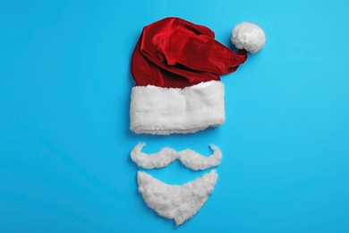 Santa Claus hat and beard on light blue background, flat lay