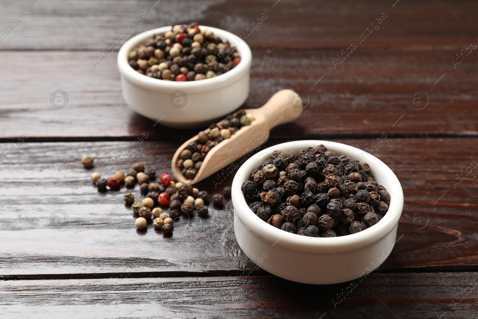 Photo of Aromatic spice. Different peppers in bowl and scoop on wooden table