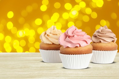 Image of Delicious birthday cupcakes on white wooden table against blurred lights. Space for text