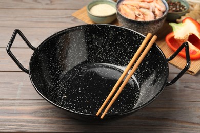 Photo of Black wok, chopsticks and products on color wooden table, closeup