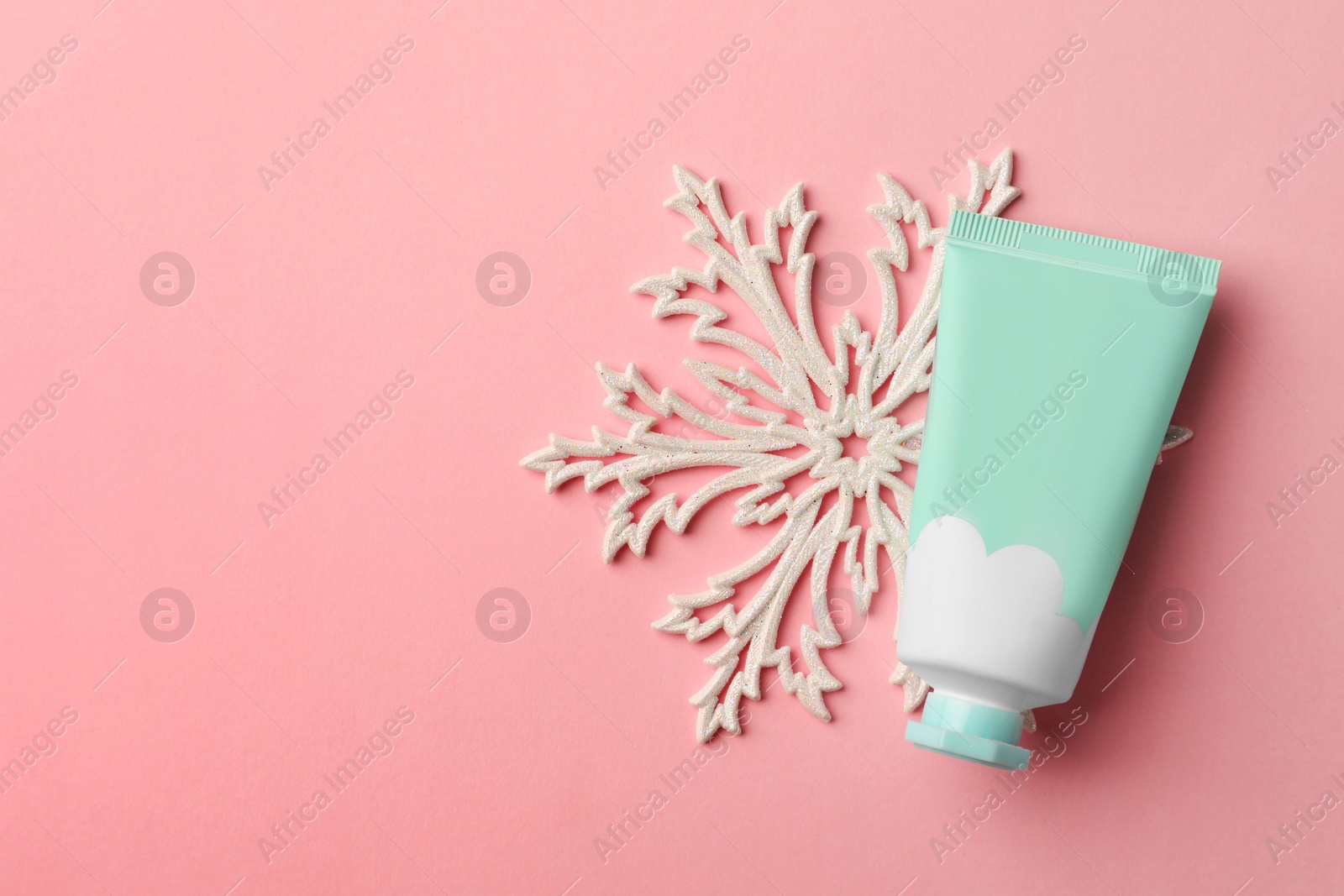 Photo of Winter skin care. Hand cream and snowflake on pink background, top view. Space for text
