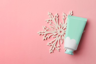 Winter skin care. Hand cream and snowflake on pink background, top view. Space for text