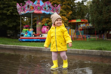 Happy little girl walking in puddle near carousel outdoors