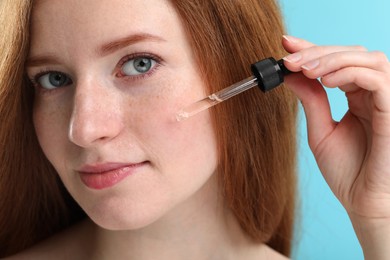 Photo of Beautiful woman with freckles applying cosmetic serum onto her face against light blue background, closeup