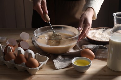 Woman making dough with whisk in bowl at table, closeup