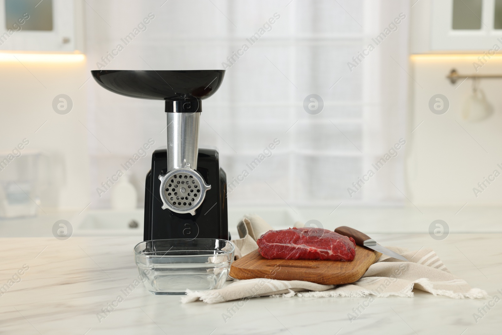 Photo of Electric meat grinder with beef on white marble table in kitchen