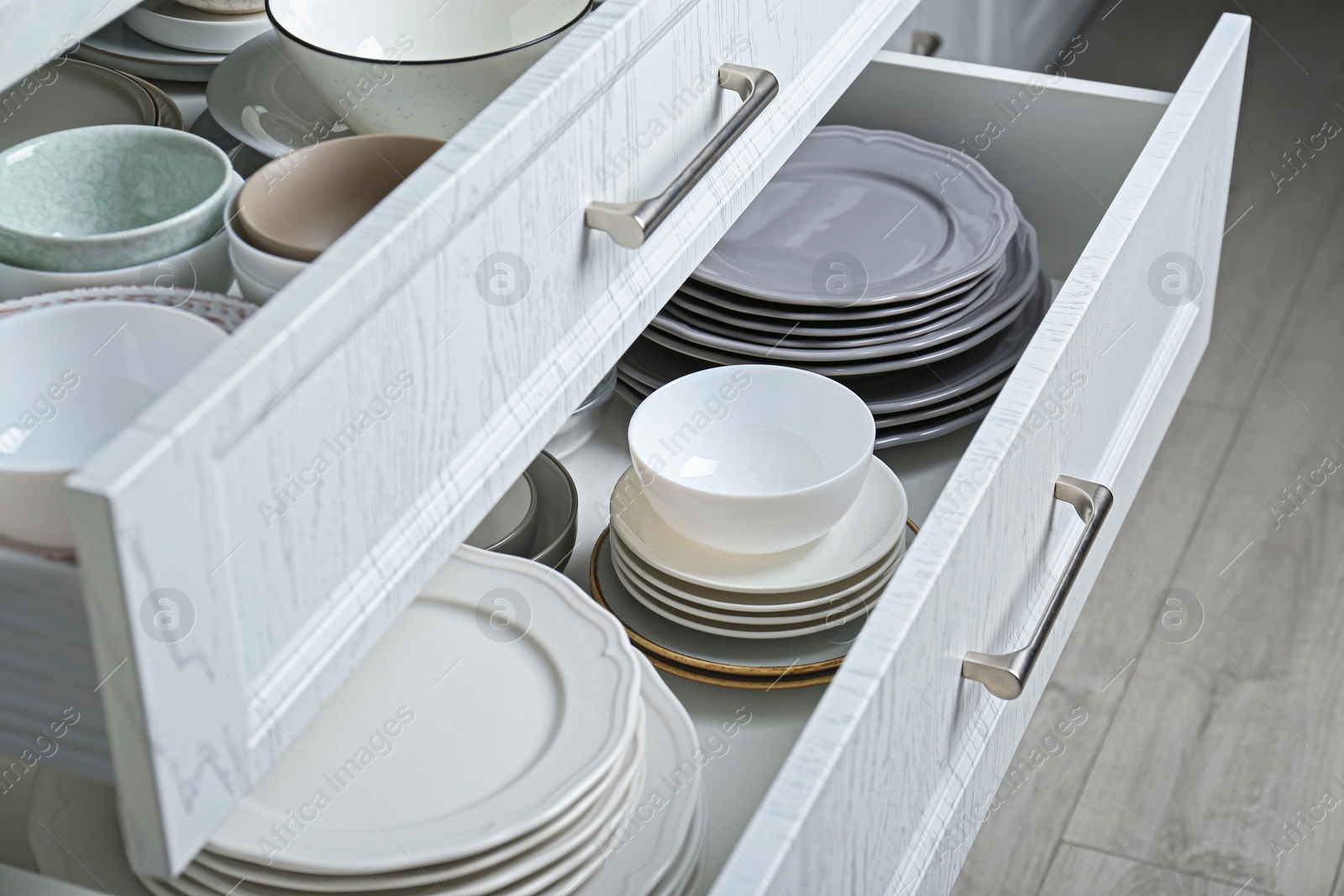 Photo of Open drawers with different plates and bowls in kitchen, closeup