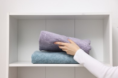 Photo of Woman stacking clean towels on shelf indoors, closeup