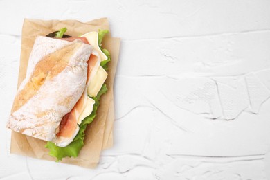Photo of Tasty sandwich with brie cheese and prosciutto on white textured table, top view. Space for text