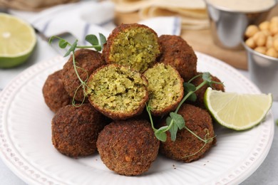 Photo of Delicious falafel balls, lime and microgreens on table, closeup