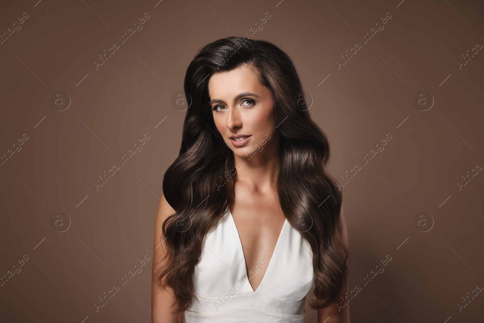 Image of Gorgeous woman with shiny wavy hair on brown background. Professional hairstyling