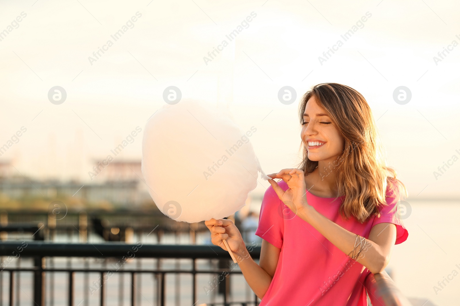 Photo of Happy young woman with cotton candy on waterfront